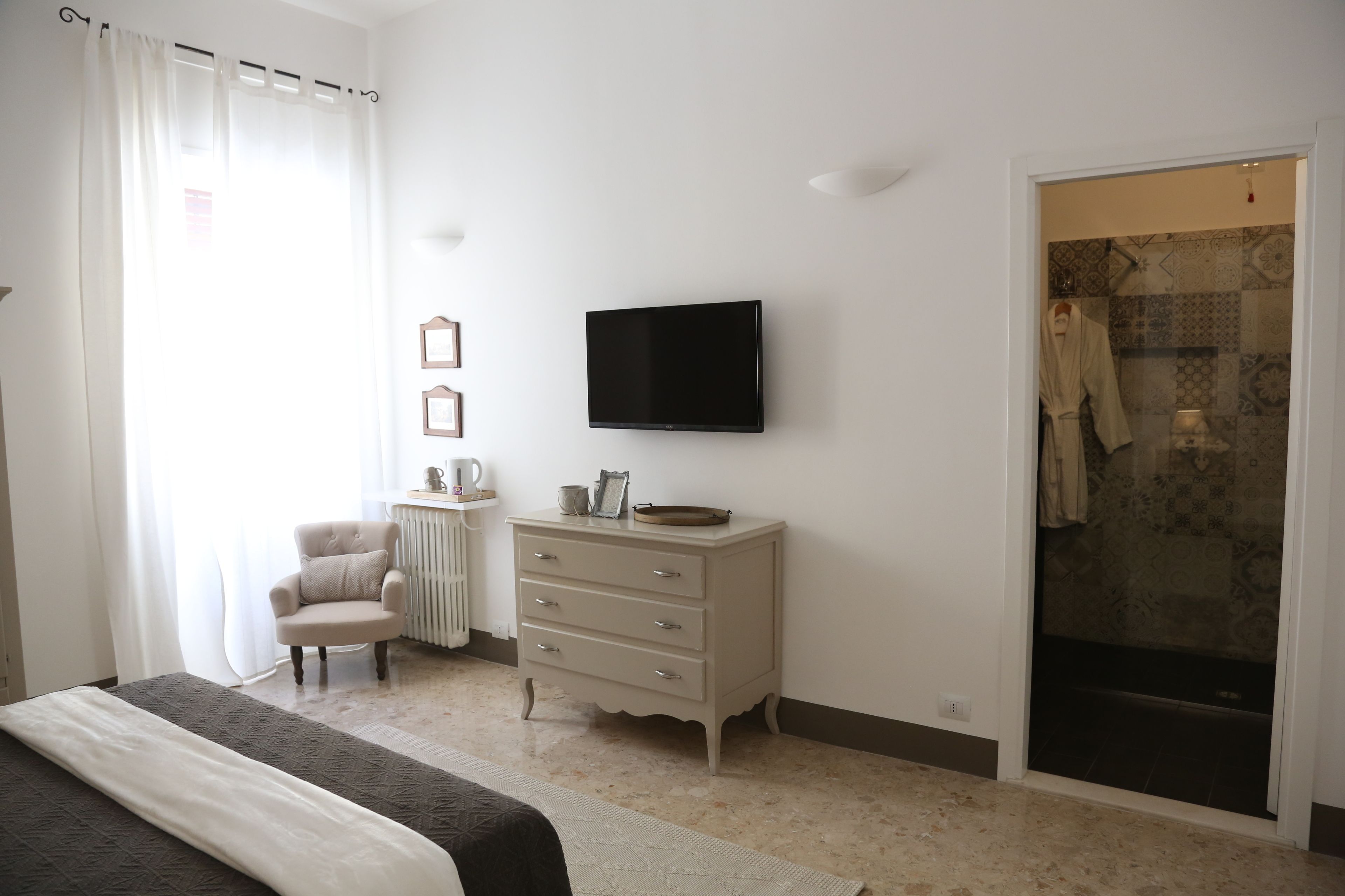 A bedroom with a bed, a dresser, a television, a chair, and a shower area.