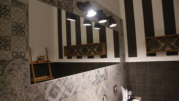 A bathroom with patterned tiles, a mirror, and a shelf with decorative items.