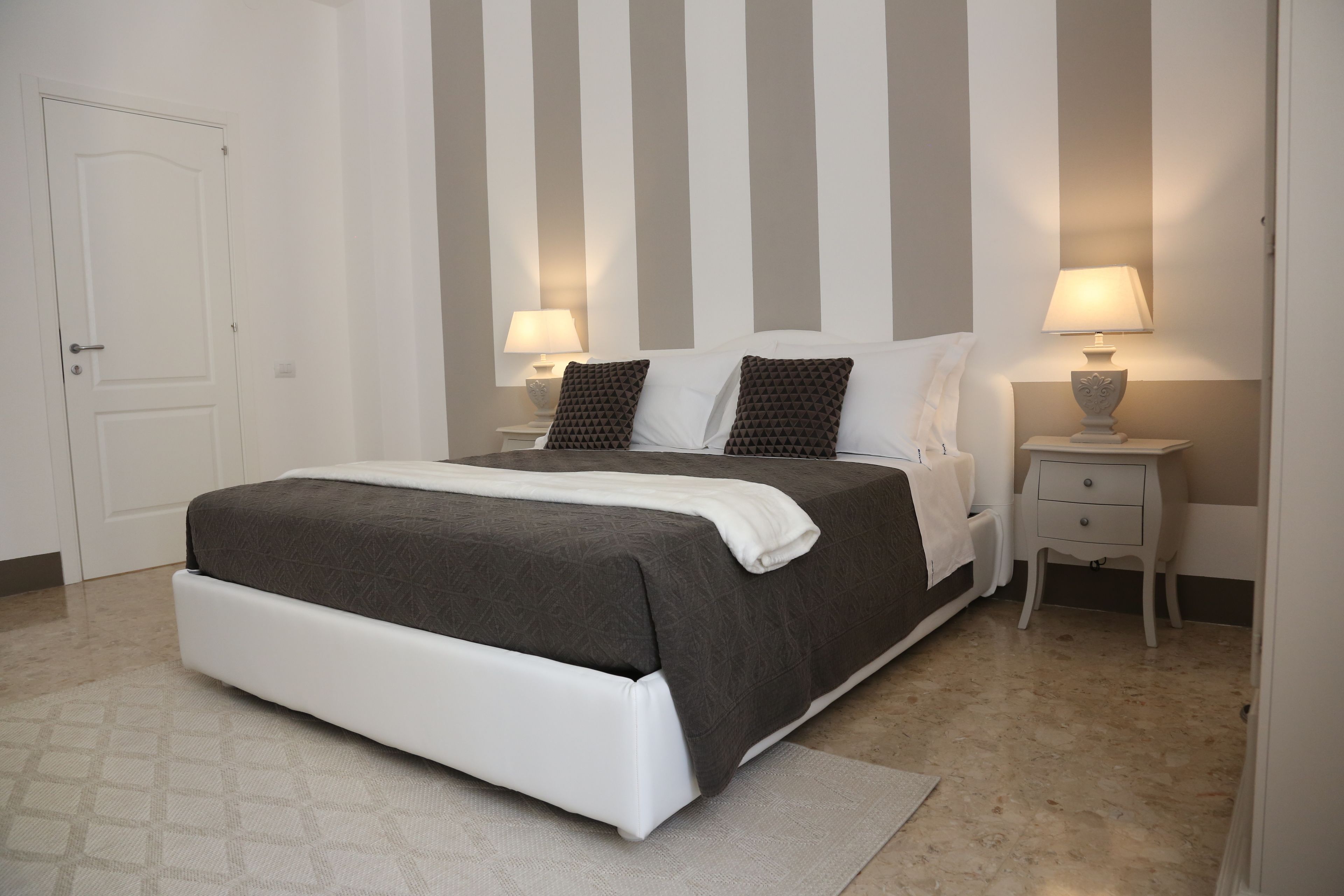 A bedroom with a bed, two bedside tables with lamps, a door, and a striped wall.
