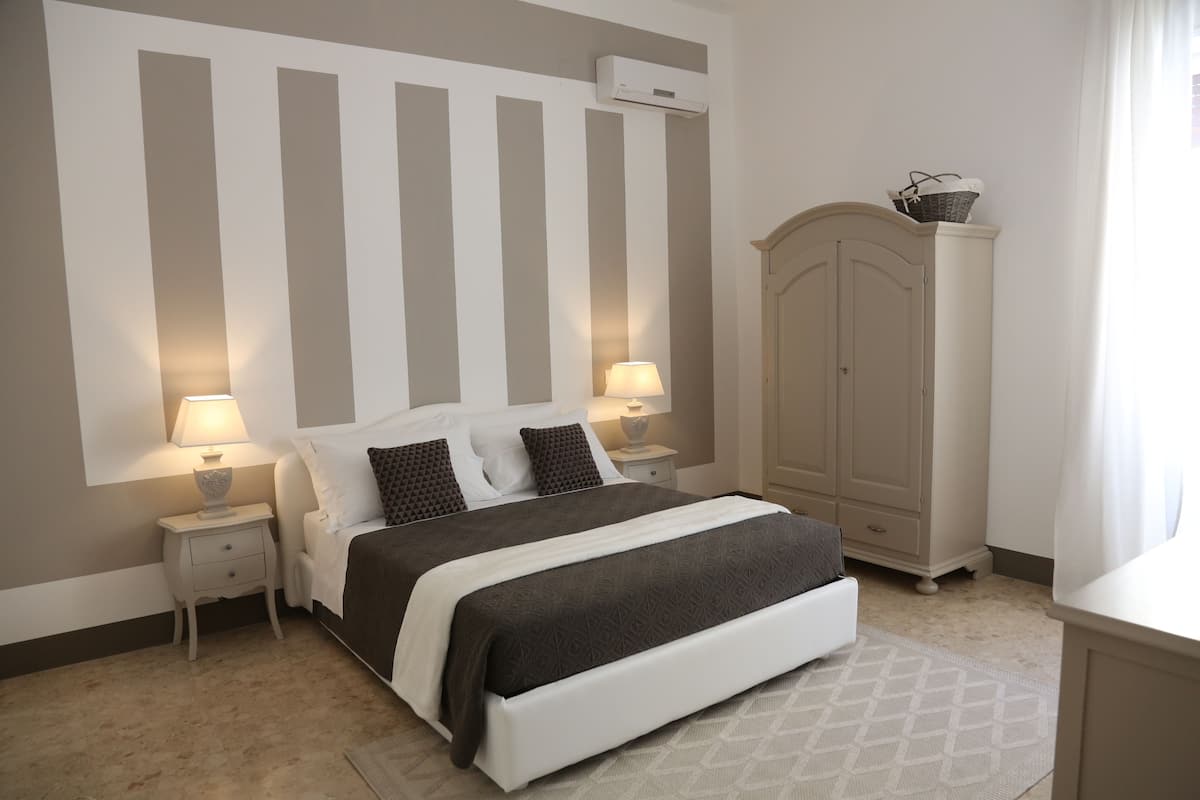 A bedroom with a large bed, two bedside tables with lamps, a wardrobe, and a window with curtains.