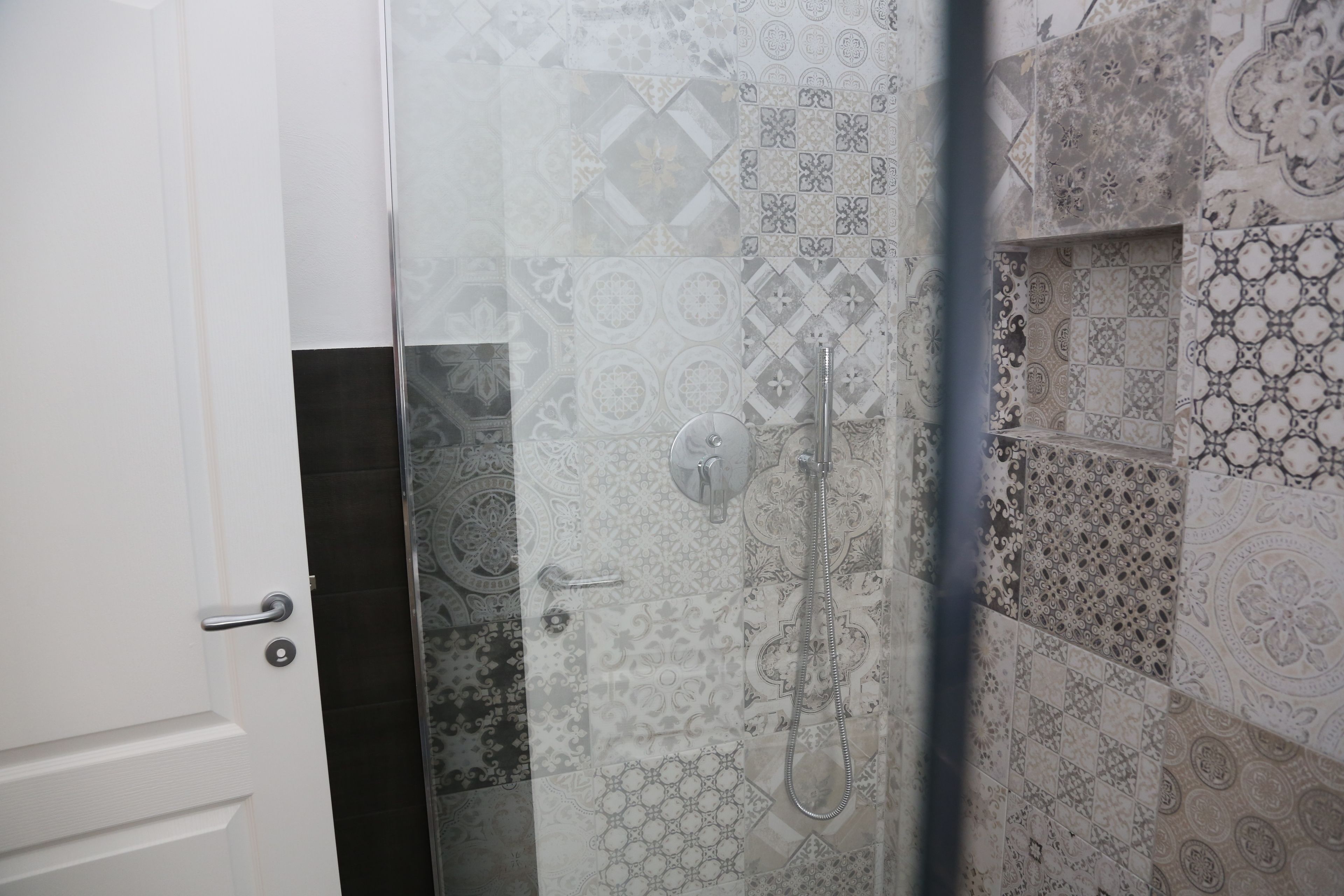 A bathroom with patterned tiles, a glass shower enclosure, and a white door.
