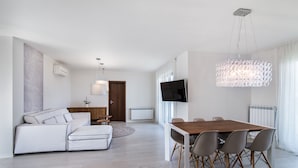 Un salon moderne comprenant un canapé, une table à manger et des chaises, un téléviseur fixé au mur et un lustre.