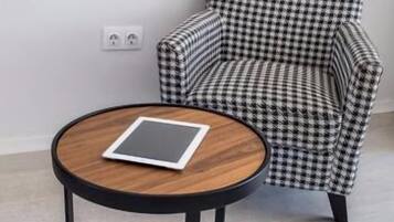 A round wooden table with a tablet on it, positioned in front of a houndstooth patterned armchair.