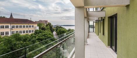 Varanda com guarda-corpo de vidro com vista para a paisagem urbana e vegetação.