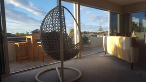 A balcony with a hanging chair, a sofa, and a view of the surrounding area. - Apartment by The Beach (Tauranga)