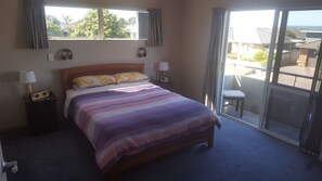 A bedroom with a bed, bedside lamps, a radio, and a view of the outside through a sliding door. - Apartment by The Beach (Tauranga)