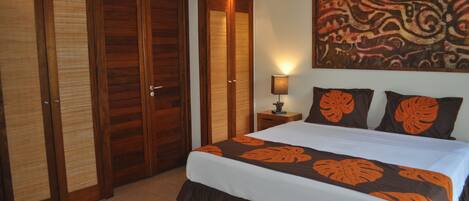 A bedroom with a large bed, wooden wardrobe, and a wall painting.