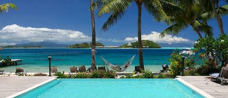 A pool area with lounge chairs and a hammock, overlooking a turquoise sea and a distant island.