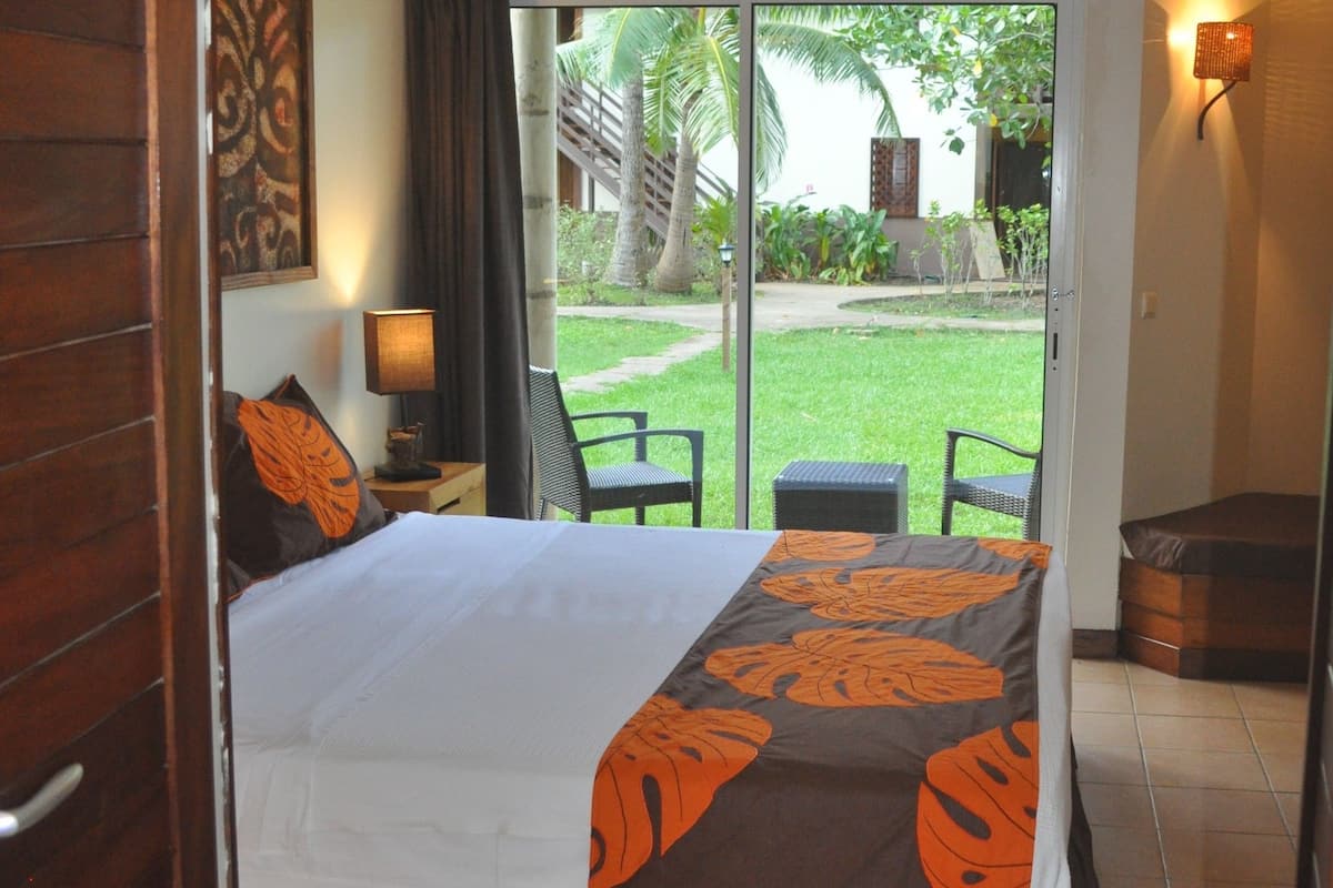A hotel room with a bed, a desk, a chair, and a view of the outdoor garden.