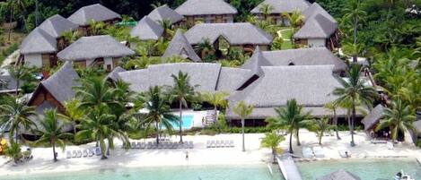 A resort with thatched-roof bungalows surrounded by palm trees and a clear turquoise sea.