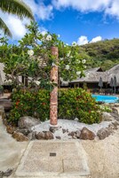 A tropical resort with a thatched-roof building, a pool, and a tiki-style pillar.