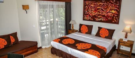 A bedroom with a bed, a sofa, a chair, a nightstand, a lamp, and a window with curtains.
