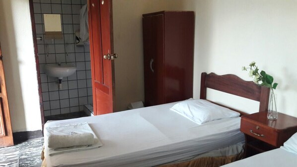 A hotel room with a bed, a wooden wardrobe, a bedside table with a vase, and a bathroom with a sink and tiled walls. - Hotel Yeland (Nagarote)