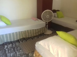 Habitación de hotel con dos camas, un ventilador de pie y una mesita con un objeto rosa.