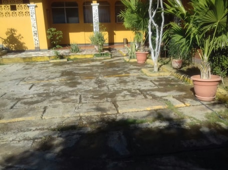 A courtyard with potted plants, a yellow building, and a stone floor.