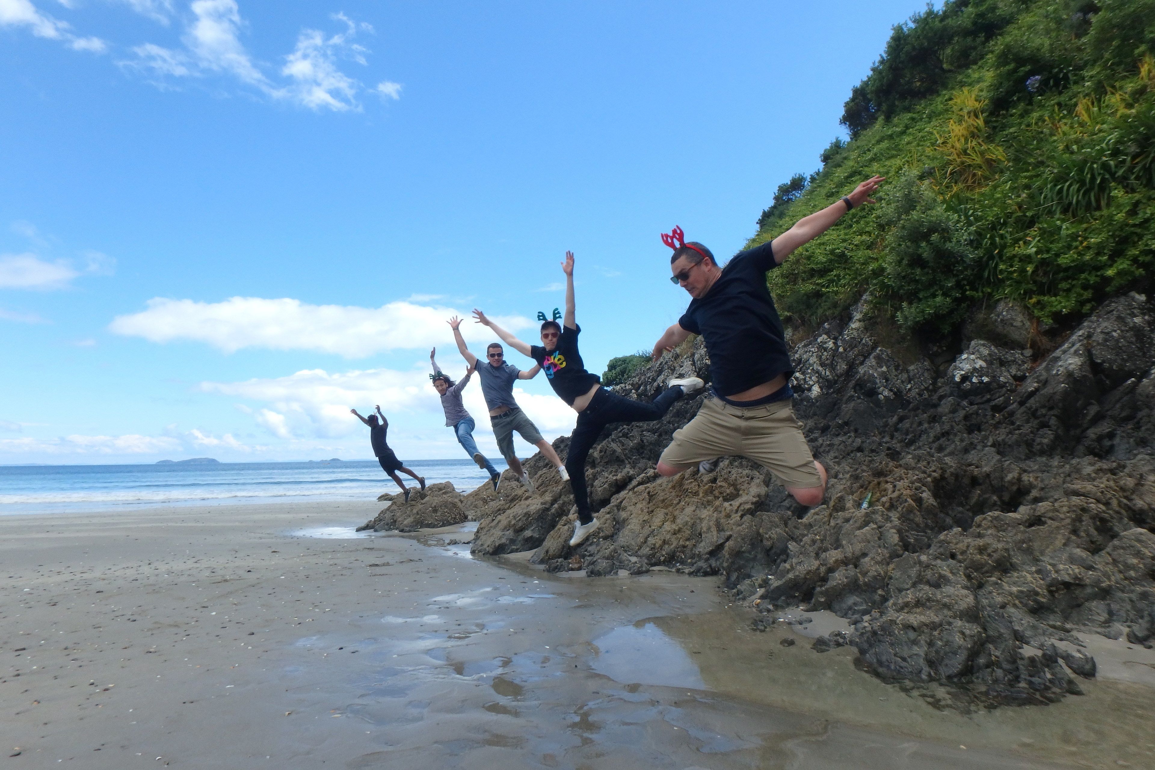 Un grupo de personas saltando desde rocas a la playa.