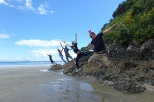 Eine Gruppe von Menschen springt von Felsen an einen Strand.