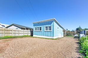 A small, single-story house with a blue exterior and white trim, surrounded by a gravel driveway and a wooden fence. - The Little Blue Bach in Oneroa Village (Waiheke Island)