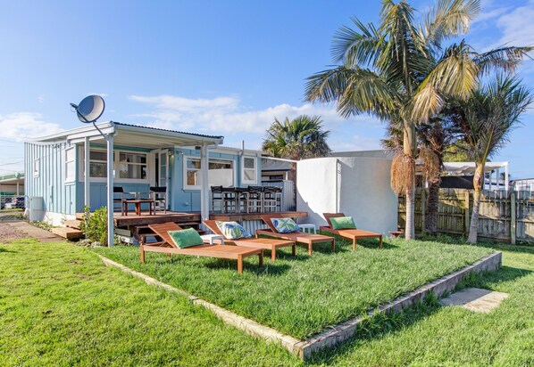 A house with a covered patio area, outdoor furniture, and a satellite dish. - The Little Blue Bach in Oneroa Village (Waiheke Island)