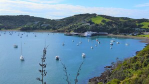 A coastal bay with numerous boats anchored, a pier, and a backdrop of green hills. - Ted's Cottage near Little Oneroa Beach (Waiheke Island)