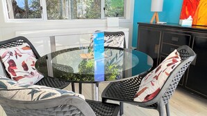 Uma mesa redonda de vidro com quatro cadeiras, cada uma com uma almofada floral. Um sinal informativo azul está sobre a mesa.