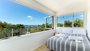Quarto com uma grande janela que oferece uma vista panorâmica de áreas verdes e uma paisagem distante.