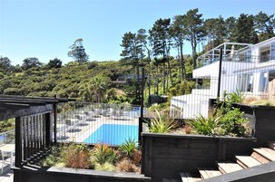 Ein moderner Poolbereich im Freien mit einem blauen Pool, umgeben von Holzterrassen und Pflanzen.