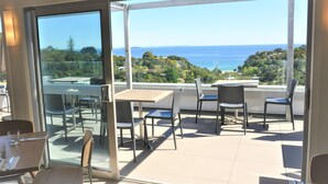 Ein Balkon mit Glastür, Sitzgelegenheit im Freien und Blick auf Meer und Grünflächen.