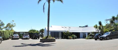 A building with a white facade, a paved driveway, and several parked cars.