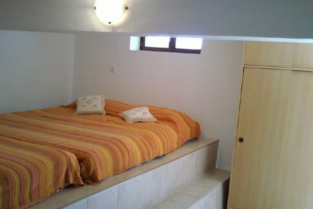 A bedroom with a bed, two pillows, a wooden wardrobe, and a small window.