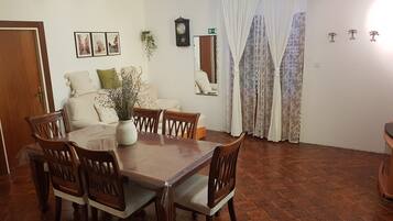 Un comedor con una mesa y sillas de madera, un jarrón con flores, un reloj en la pared y una ventana con cortinas.