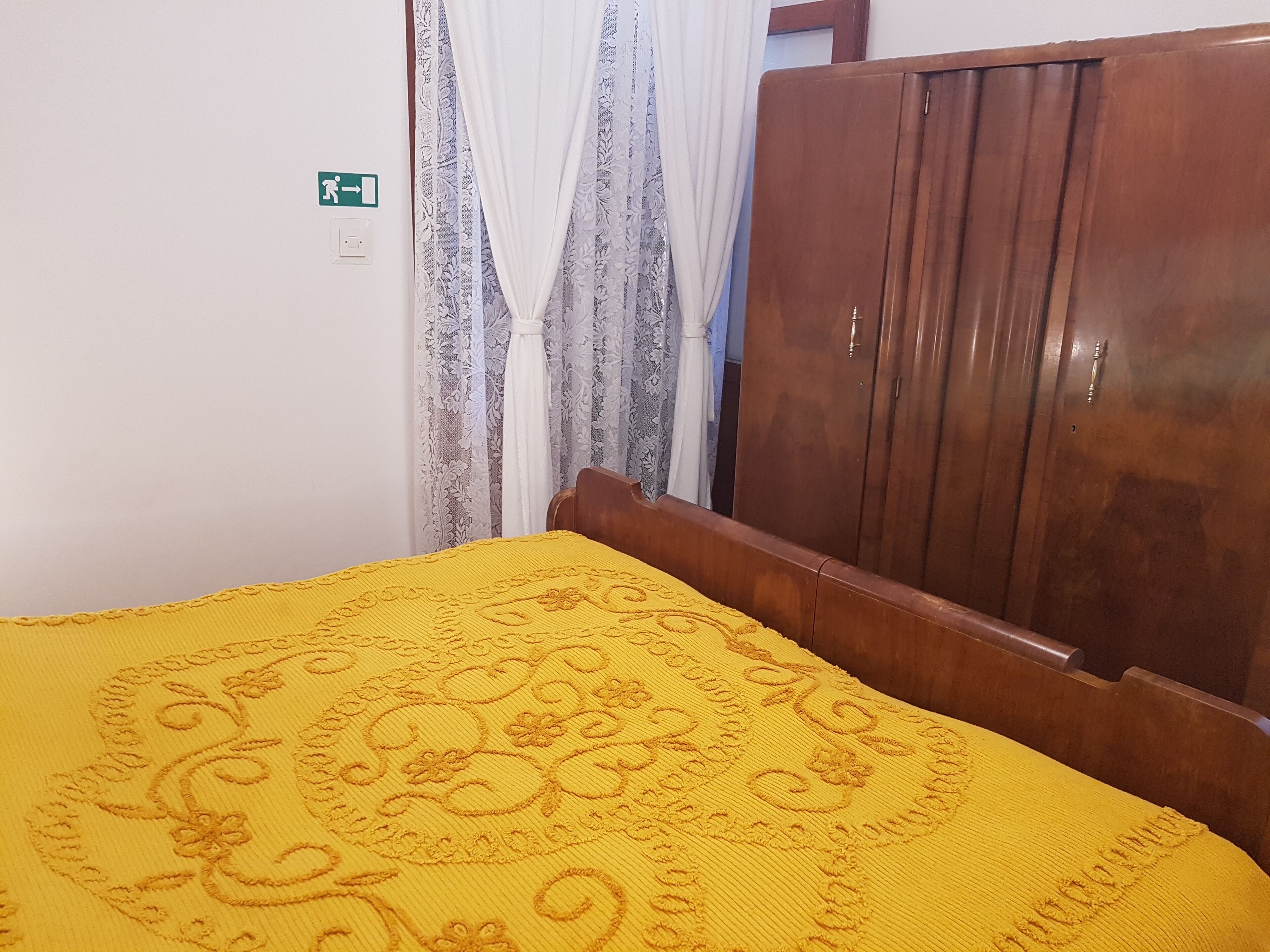 A room with a bed, a wooden wardrobe, and a curtain.