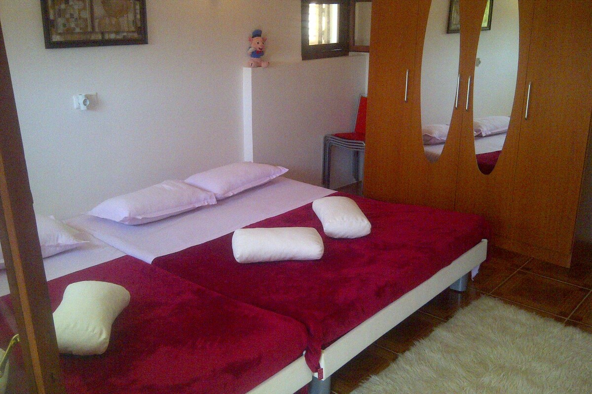 Un dormitorio con cama, almohadas, una manta roja, una mesita y un espejo.