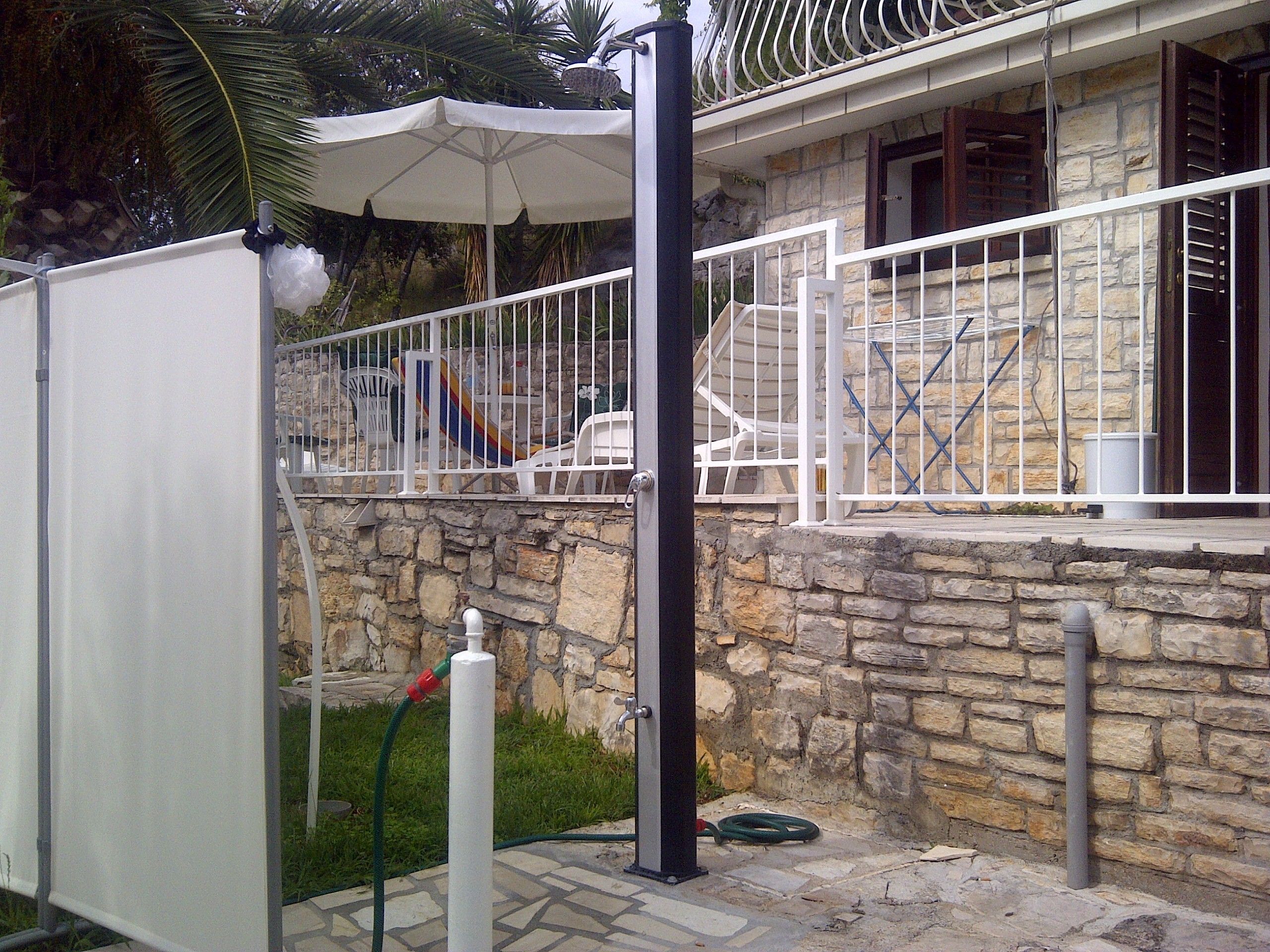 A stone building with a white balcony, a metal gate, and a white umbrella.