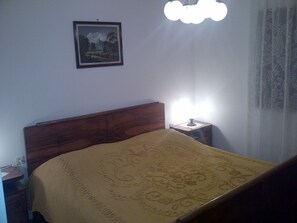 Un dormitorio con cabecera de madera, mesita de noche con lámpara y un cuadro enmarcado en la pared.