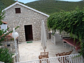 Un edificio de piedra con un patio adoquinado, una puerta y un pequeño ventanal. Se observan sillas de mimbre y una mesa con mantel rojo.
