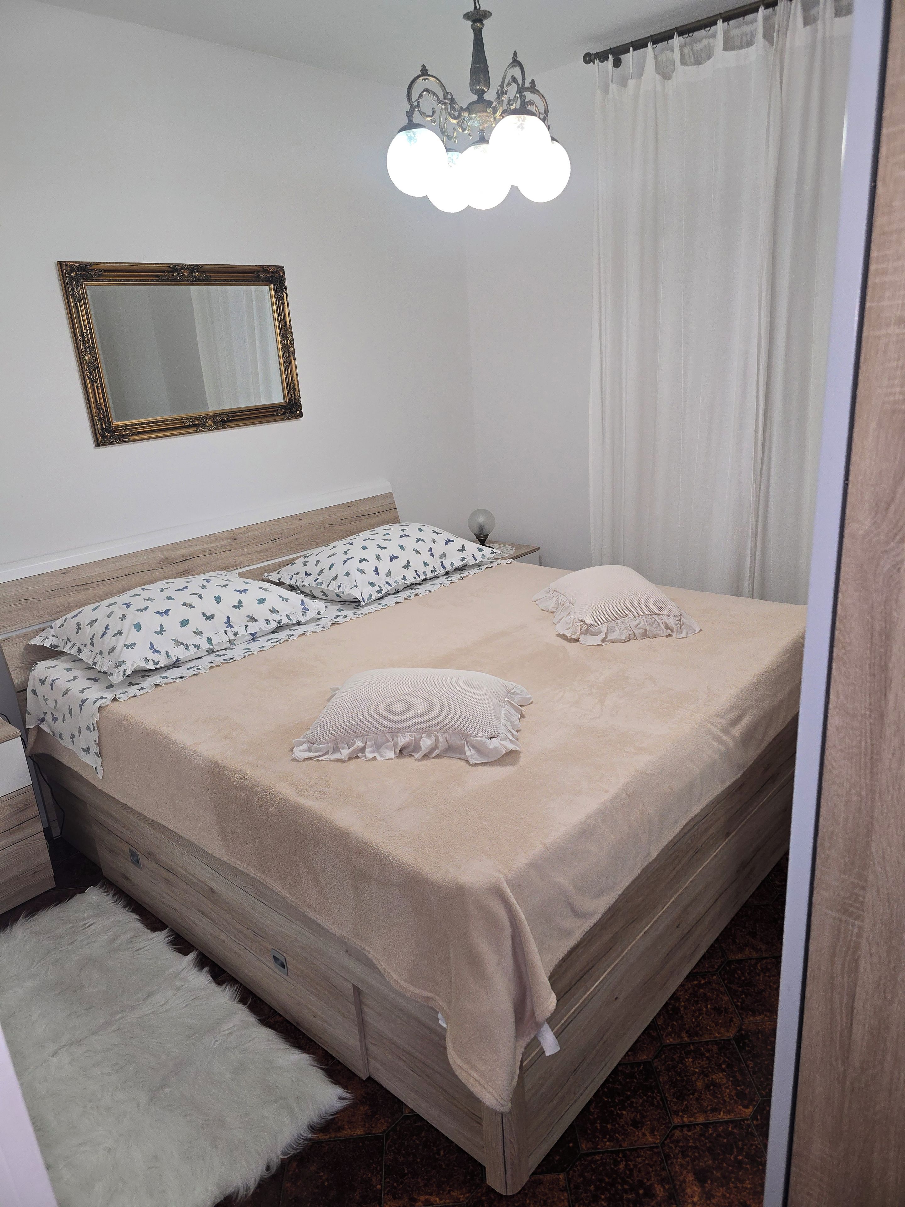 A bedroom with a bed, a nightstand, a mirror, and a chandelier.