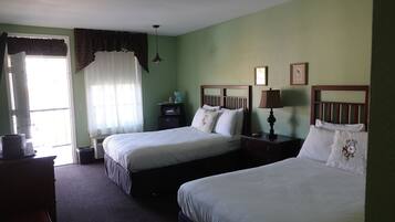 A hotel room with two single beds, a dresser, a desk with a lamp, and a window with curtains.