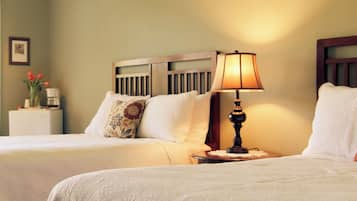 Een hotelkamer met twee bedden, een nachtkastje met een lamp en een kleintje tafeltje met een bloemenvaas.