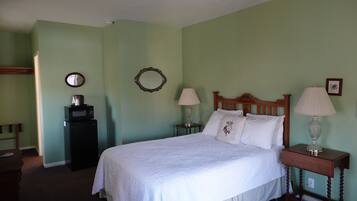 A bedroom with a bed, two bedside tables with lamps, a dresser, a microwave, and a mirror on the wall.