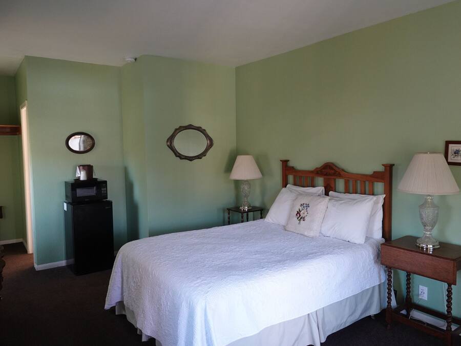 A bedroom with a bed, two bedside tables with lamps, a dresser, a microwave, and a mirror on the wall.
