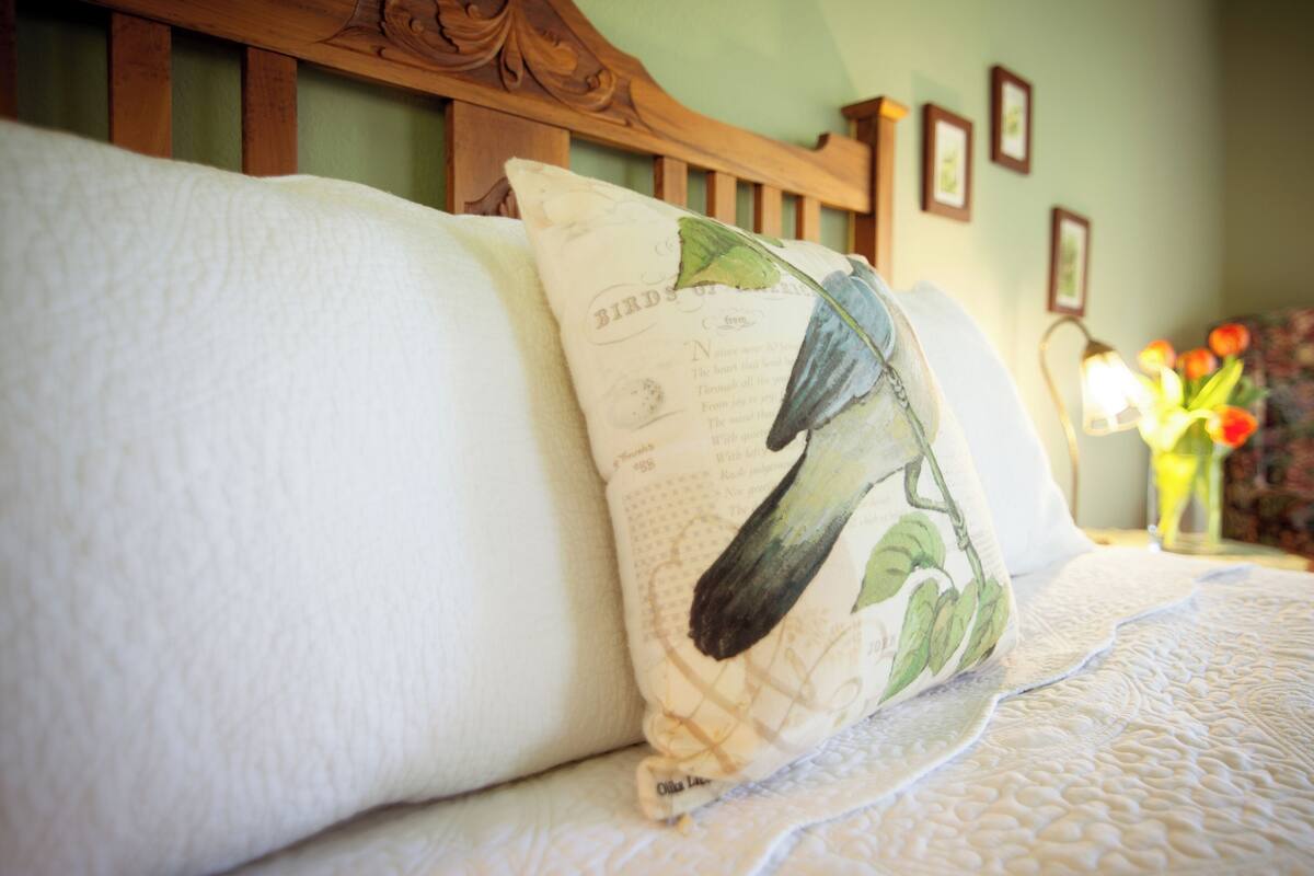 Una cama con colcha blanca y almohada con ilustración de un pájaro.