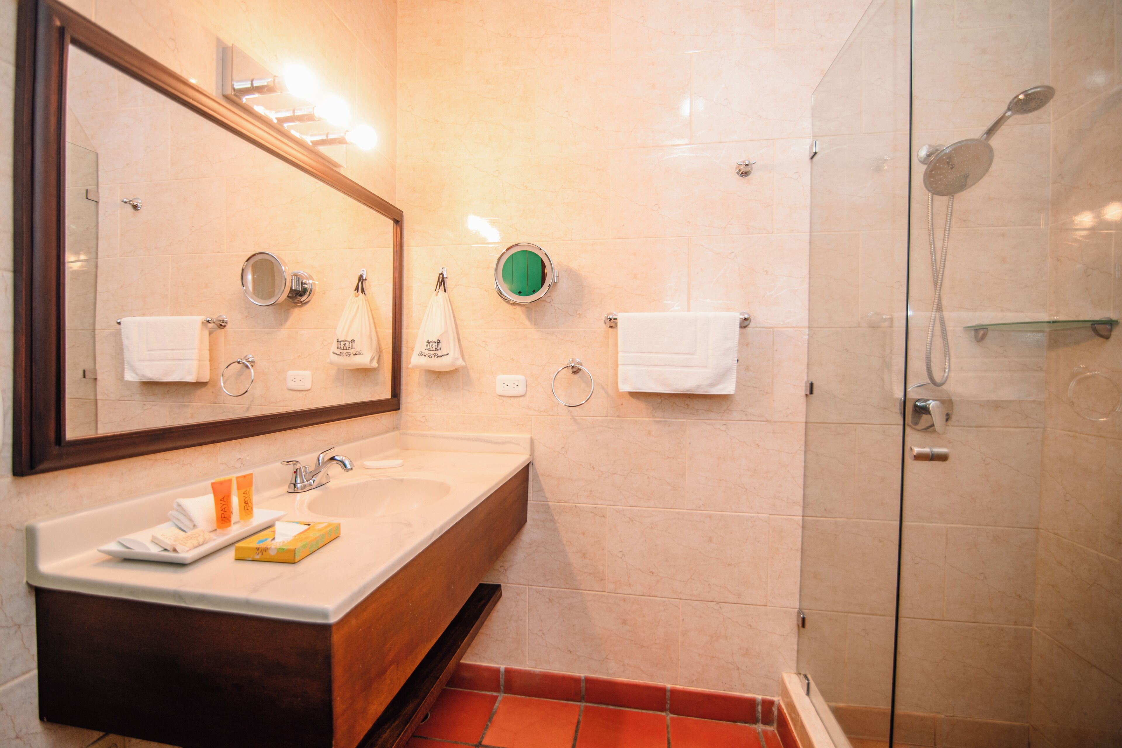 Un baño con lavamanos, espejo, toallero y ducha.