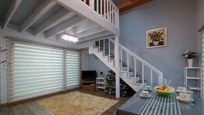 A spacious living area with a staircase, a dining table with a checkered tablecloth, and a television in the background. - Tirol Pension (Pyeongchang)
