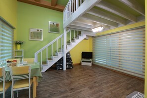 A dining area with a table set for two, a staircase, and a television on a stand.
