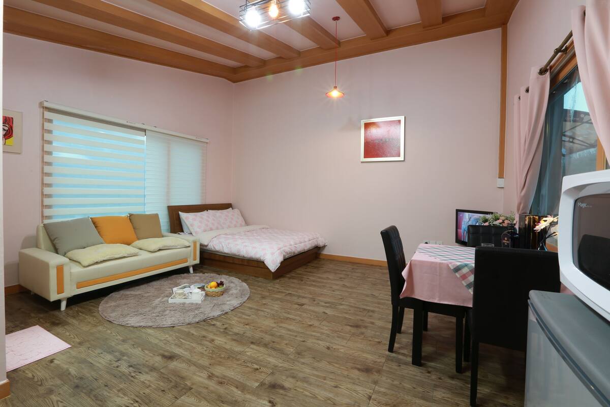 A cozy room with a bed, a sofa, a dining table with chairs, and a television.