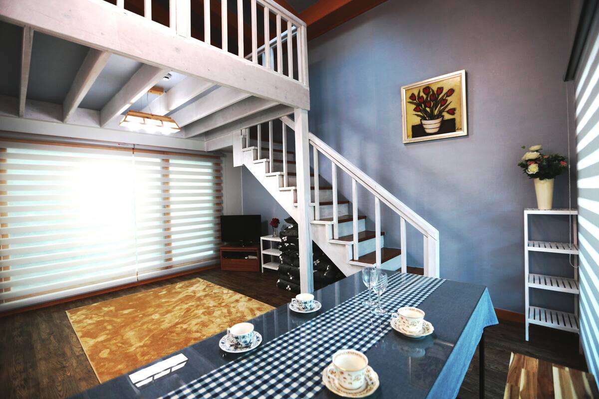 A room with a checkered tablecloth, a staircase, a television, and a potted plant.