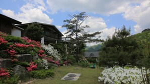 A garden with a pathway, a wooden house, and a mountain in the background. - Tirol Pension (Pyeongchang)