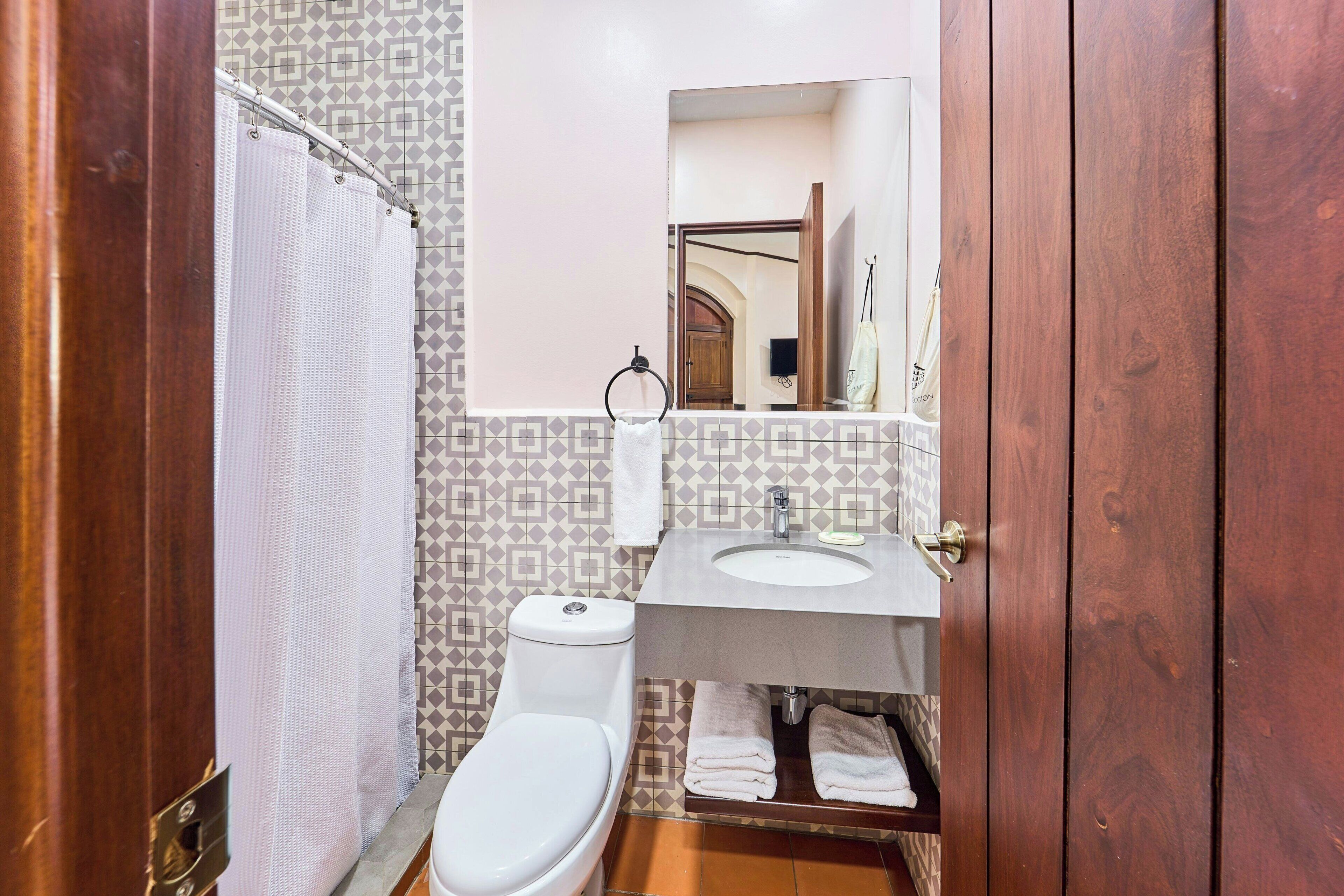 Un baño con inodoro, cortina de ducha, lavabo y espejo.
