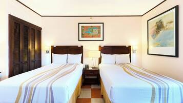 A hotel room with two beds, a nightstand, a lamp, and artwork on the walls.